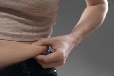 Photo of Woman touching belly fat on grey background, closeup. Overweight problem