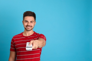 Photo of Happy young man operating air conditioner with remote control on light blue background. Space for text