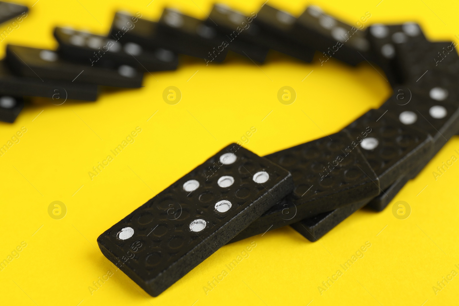 Photo of Falling black domino tiles on yellow background