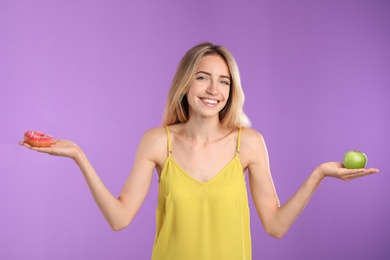 Photo of Woman choosing between doughnut and healthy apple on violet background