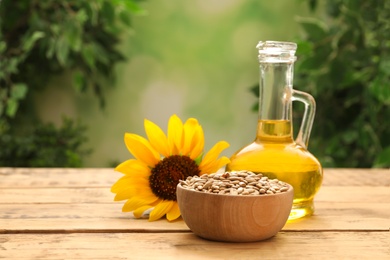 Photo of Sunflower, jug of oil and seeds on wooden table against blurred background