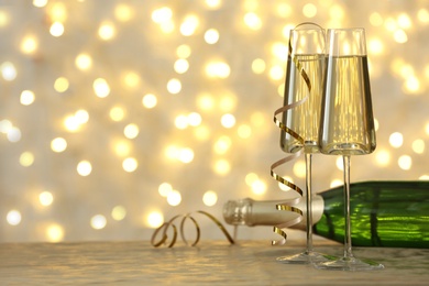 Photo of Glasses and bottle of champagne on table against blurred lights. Space for text