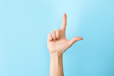 Photo of Woman showing L letter on color background, closeup. Sign language