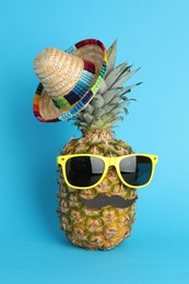 Photo of Pineapple with Mexican sombrero hat, sunglasses and fake mustache on light blue background