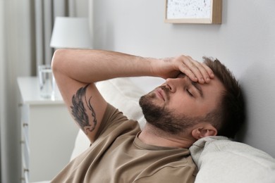 Photo of Young man suffering from migraine at home