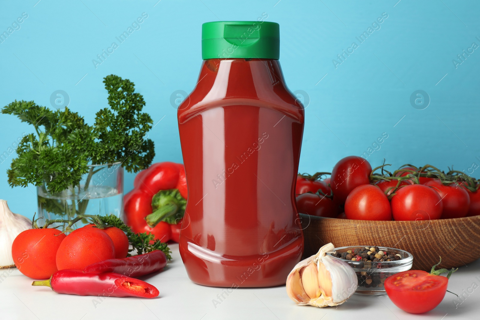 Bottle of tasty ketchup and ingredients on white marble table Photo of Bottle of tasty ketchup and ingredients on white marble table