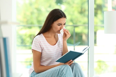 Young woman with book suffering from allergy at home