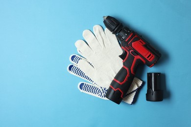 Photo of Electric screwdriver and gloves on light blue background, top view
