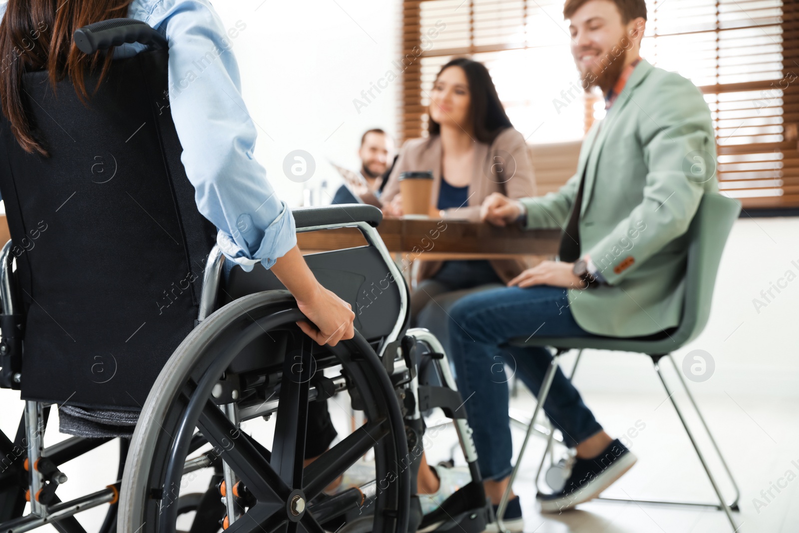 Photo of Young woman in wheelchair with colleagues at office, closeup