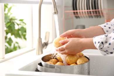 Photo of Woman washing fresh potatoes in kitchen sink, closeup