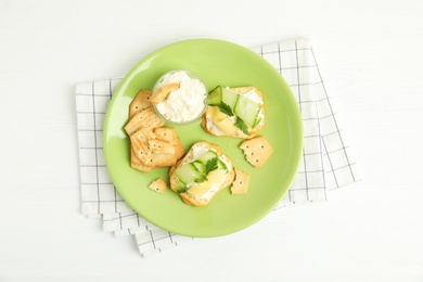 Photo of Delicious crackers with cream cheese, cucumber and parsley on white wooden table, top view