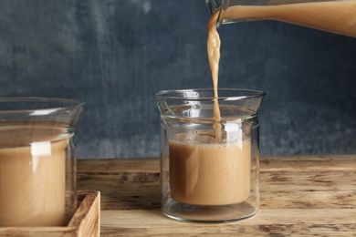 Photo of Pouring tasty coffee into glass cup on wooden table