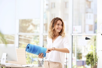 Photo of Young beautiful businesswoman holding yoga mat in office. Gym after work