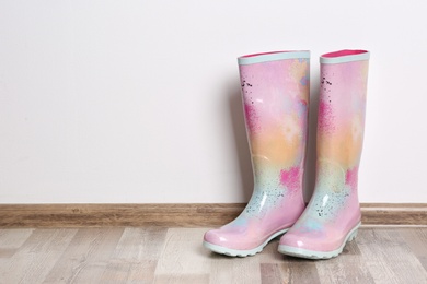 Photo of Pair of gumboots on wooden floor against white wall. Female shoes