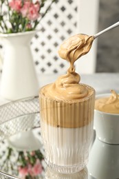 Photo of Pouring cream for dalgona coffee into glass on mirror tray, closeup