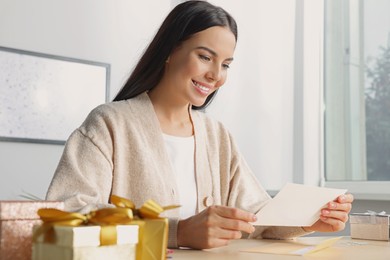 Photo of Happy woman reading greeting card at wooden table in room