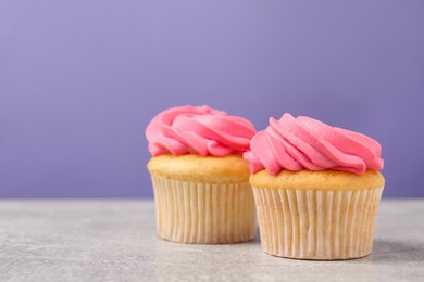 Photo of Delicious cupcakes with bright cream on gray table against violet background, space for text