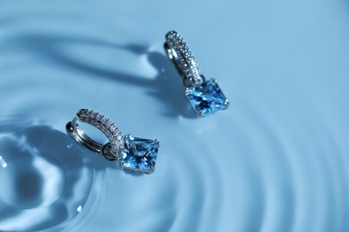 Photo of Luxury jewelry. Elegant earrings in water on light blue background, space for text