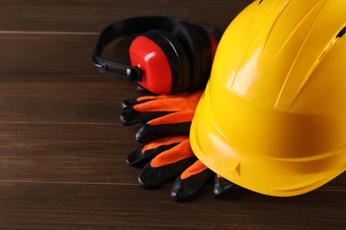 Photo of Hard hat, earmuffs and gloves on wooden table, space for text. Safety equipment