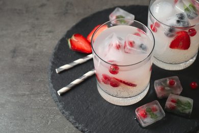 Photo of Glasses of refreshing drink with ice cubes and berries on grey table, closeup