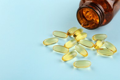 Photo of Bottle and vitamin capsules on light blue background, closeup. Space for text