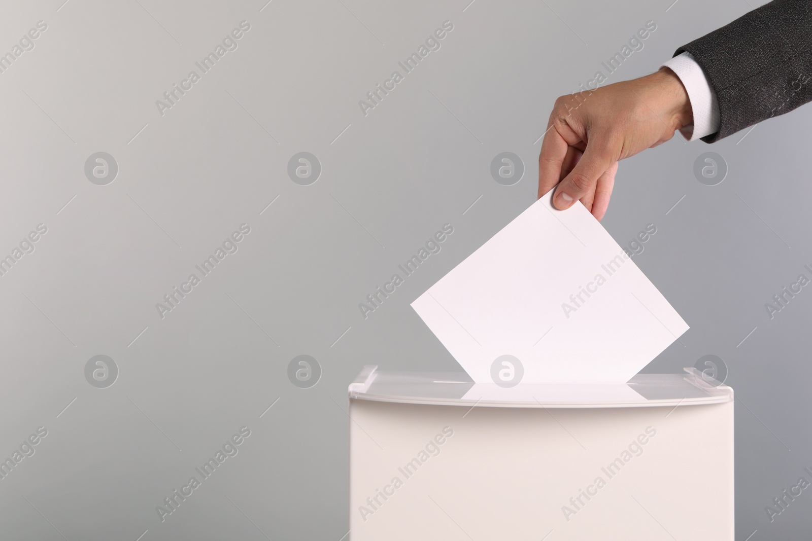 Man putting his vote into ballot box on light grey background, closeup. Space for text Photo of Man putting his vote into ballot box on light grey background, closeup. Space for text