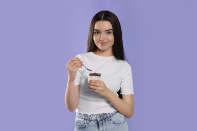 Photo of Smiling teenage girl with delicious yogurt and spoon on violet background