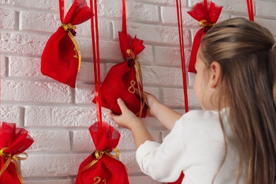 Photo of Little girl taking gift from Christmas advent calendar indoors, closeup