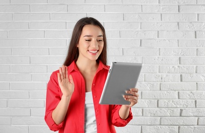 Photo of Woman using tablet for video chat against brick wall. Space for text
