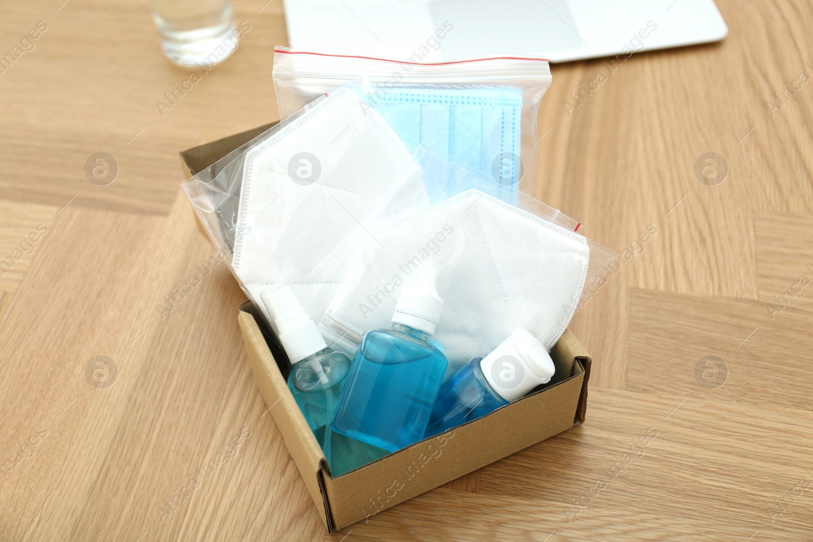 Photo of Cardboard box with antiseptics and respiratory masks on wooden table. Protective essentials during COVID-19 pandemic