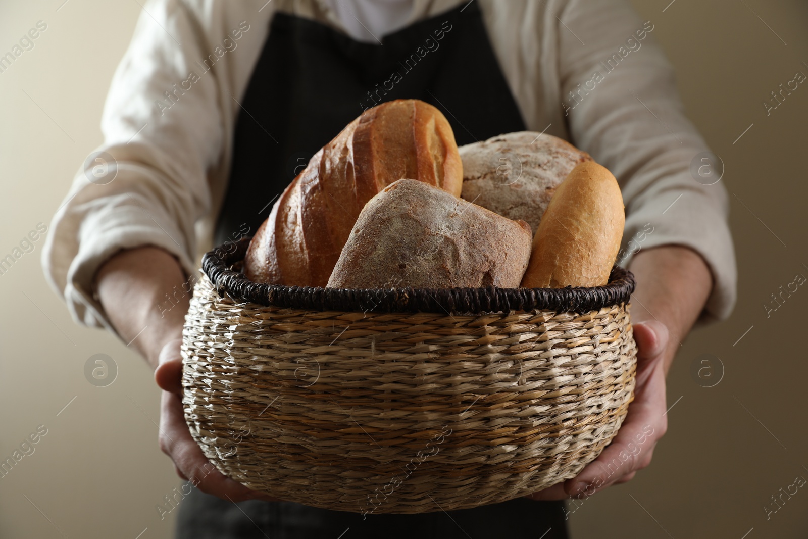 Man holding wicker basket with different types of bread on beige background, closeup Photo of Man holding wicker basket with different types of bread on beige background, closeup