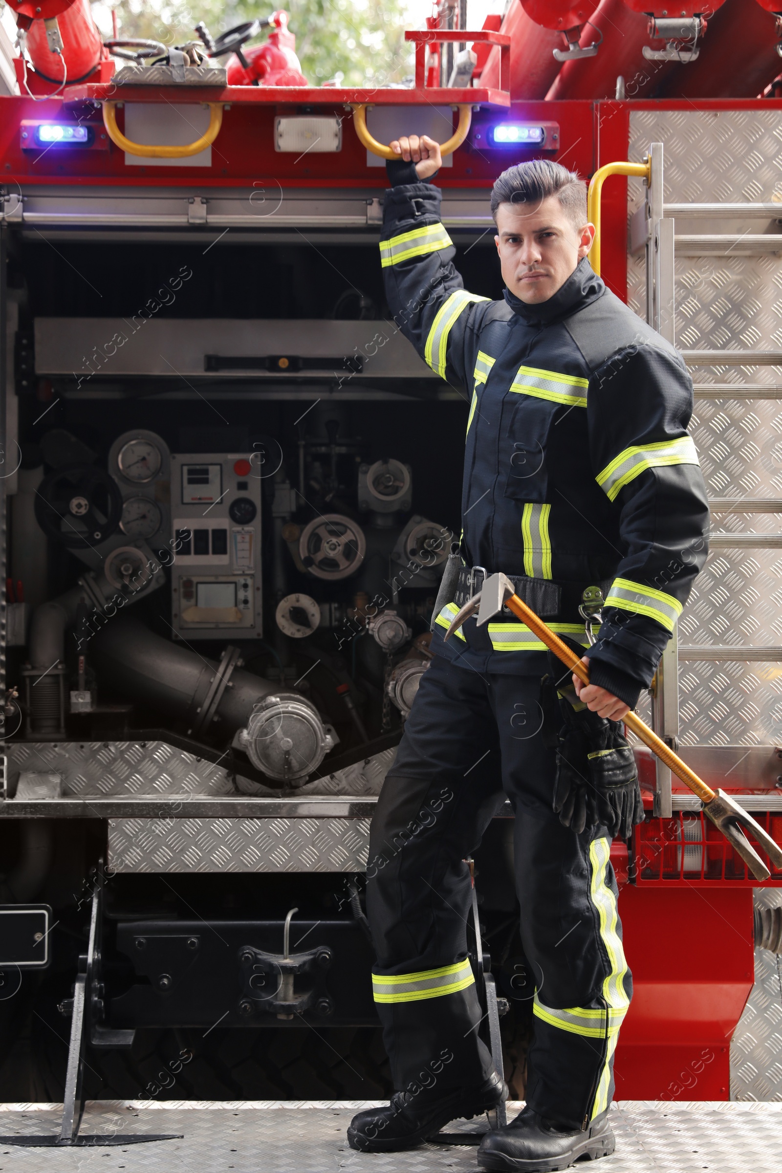 Photo of Portrait of firefighter in uniform with entry tool near fire truck outdoors