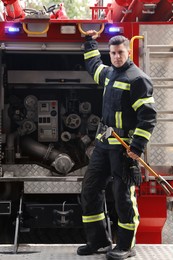 Photo of Portrait of firefighter in uniform with entry tool near fire truck outdoors