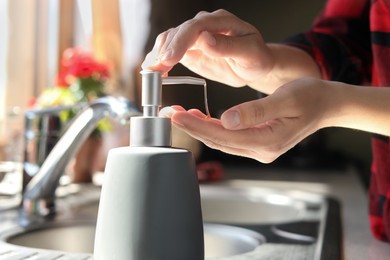 Photo of Woman using liquid soap dispenser in kitchen, closeup