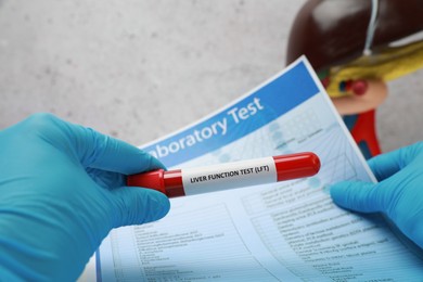 Photo of Liver Function Test. Laboratory worker holding tube with blood sample and form at table, closeup