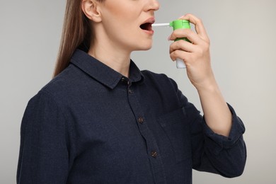 Photo of Woman using throat spray on grey background, closeup