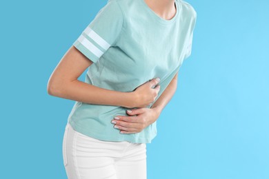 Photo of Woman suffering from stomach ache on light blue background, closeup. Food poisoning
