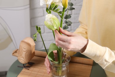 Photo of Beautiful ikebana for stylish house decor. Woman create floral composition with fresh flowers and eucalyptus branch at coffee table, closeup