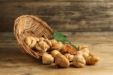 Photo of Overturned wicker basket, dried figs and green leaf on wooden table