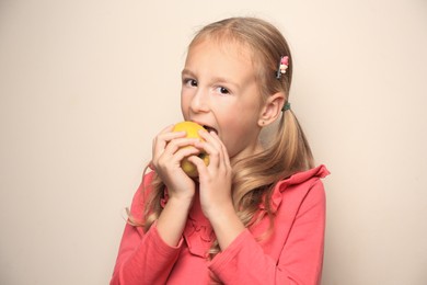 Photo of Cute little girl eating apple on light background