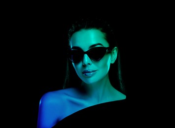 Image of Beautiful woman wearing sunglasses in neon lights against black background