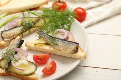 Photo of Delicious sandwiches with sprats, pickled cucumber, onion and dill served on white wooden table, closeup
