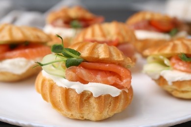 Photo of Delicious profiteroles with cream cheese and salmon on plate, closeup