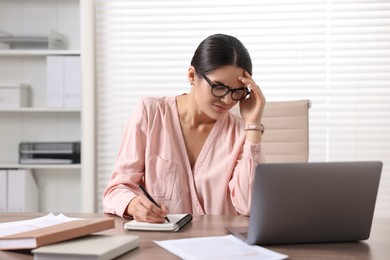 Photo of Young woman suffering from headache at wooden table in office