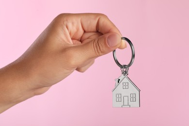 Photo of Woman holding metallic keychain in shape of house on pink background, closeup