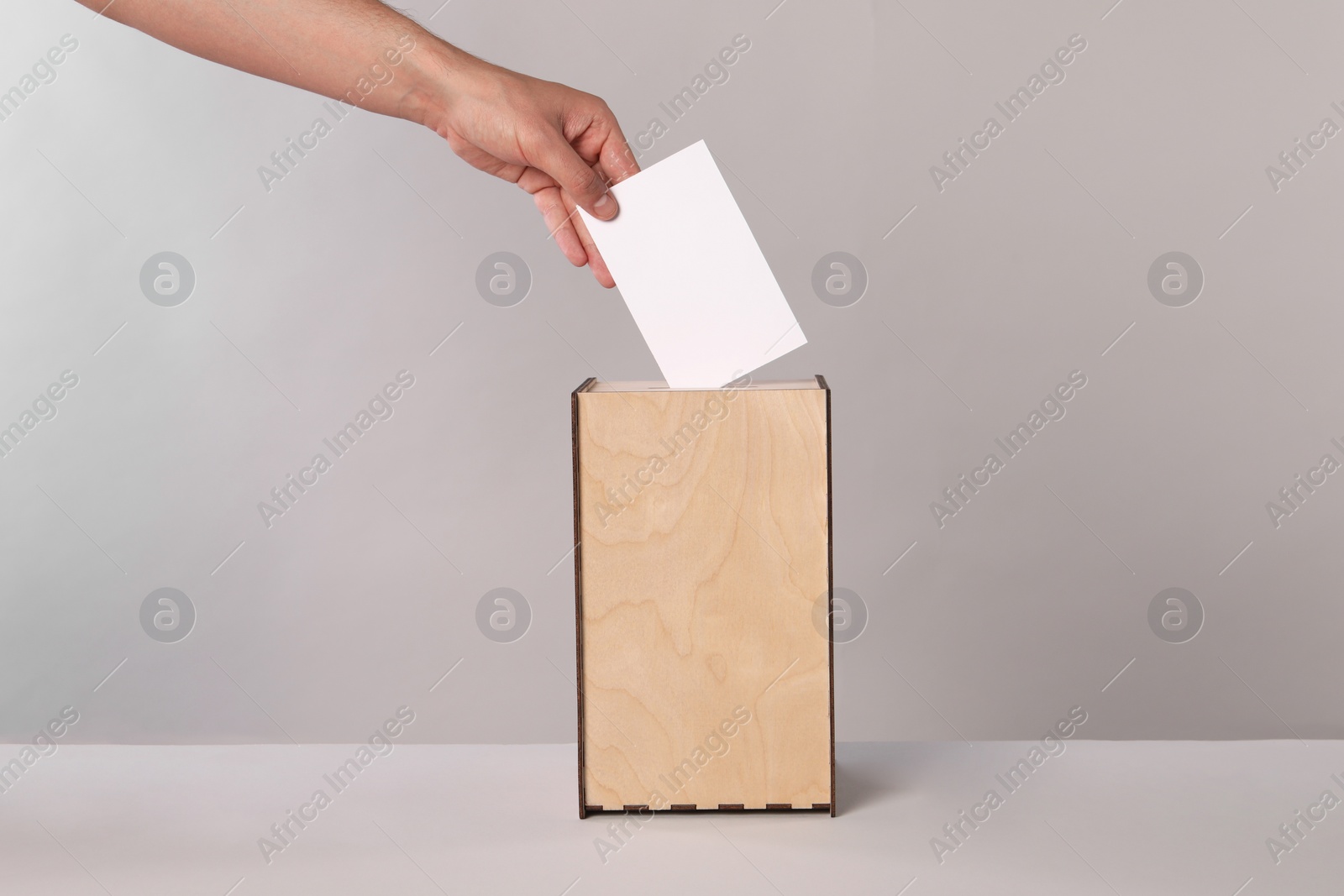 Photo of Man putting his vote into ballot box on light grey background, closeup