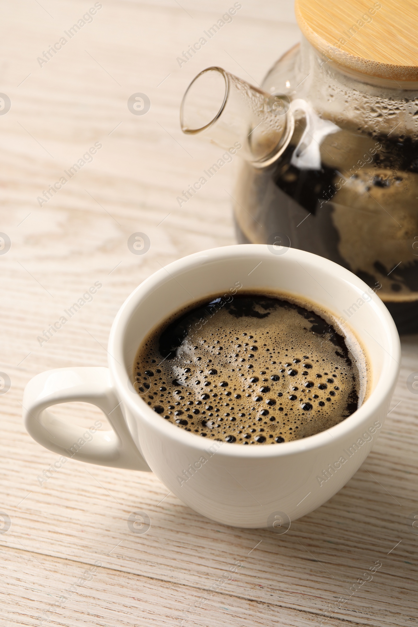 Photo of Aromatic coffee in cup and teapot on light wooden table, closeup