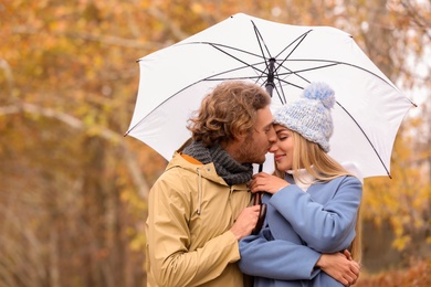 Photo of Young romantic couple with umbrella in park on autumn day