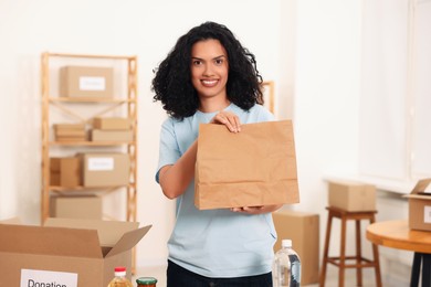 Photo of Volunteering. Happy woman with paper bag in warehouse