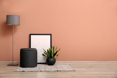 Comfortable pouf, plant, lamp and picture near pale pink wall indoors, space for text